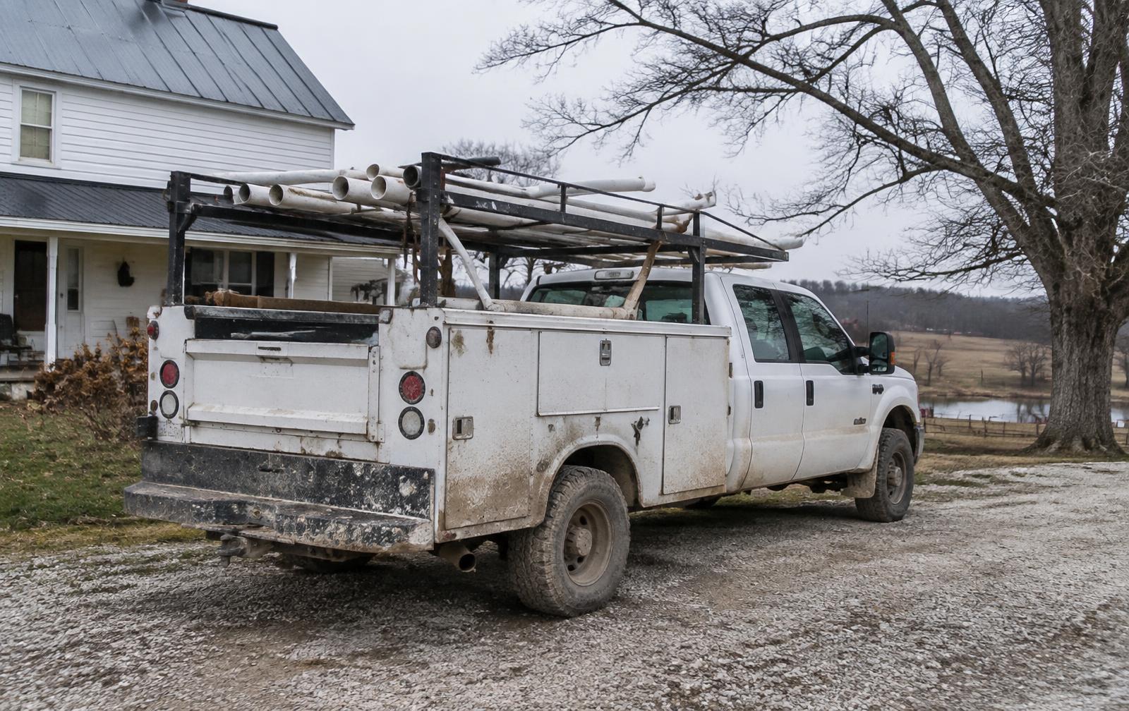 Well service truck loaded with pipe parked on a gravel farm driveway